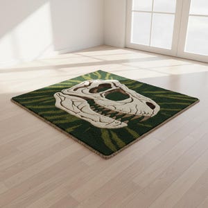 May include: A square rug with a dinosaur skull design. The rug has a green background with a striped pattern and a beige border. The skull is beige and detailed, with visible teeth and eye sockets. The rug is placed on a light wood floor.