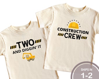May include: Two off-white toddler t-shirts. One shirt says "TWO AND DIGGIN' IT" with a yellow excavator graphic. The other shirt says "CONSTRUCTION CREW" with a yellow hard hat graphic. Both shirts have black and yellow accents.
