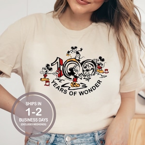 May include: A white t-shirt with a graphic of Mickey Mouse and friends celebrating 100 years of wonder. The graphic features Mickey Mouse, Minnie Mouse, Donald Duck, Goofy, and Pluto.