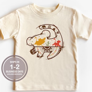 May include: A beige short-sleeved t-shirt with a brown outline of a lion's head with a tribal pattern. The lion's head is filled with images of characters from the Lion King movie, including Simba, Nala, and Timon.