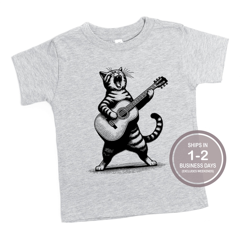 May include: A gray short-sleeved t-shirt with a black and white illustration of a cat playing a guitar. The cat is singing and has a striped tail.