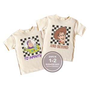 May include: Two cream-colored t-shirts featuring cartoon characters. One shirt has Buzz Lightyear in a spaceship with the text "TO INFINITY". The other shirt has Woody with the text "AND BEYOND". Both shirts have a black and white checkered background.