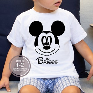 Pode incluir: Camiseta branca com uma imagem em preto e branco do Mickey Mouse com pontos de sutura na boca. O nome "Briggs" est&aacute; escrito em uma fonte cursiva preta abaixo da imagem.