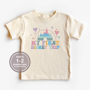 Może przedstawiać: Kremowa koszulka z kolorową grafiką zamku Kopciuszka i tekstem "My First Disney Trip".