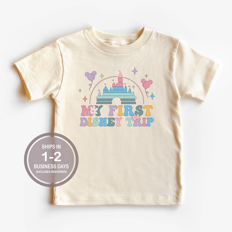 Może przedstawiać: Kremowa koszulka z kolorową grafiką zamku Kopciuszka i tekstem "My First Disney Trip".