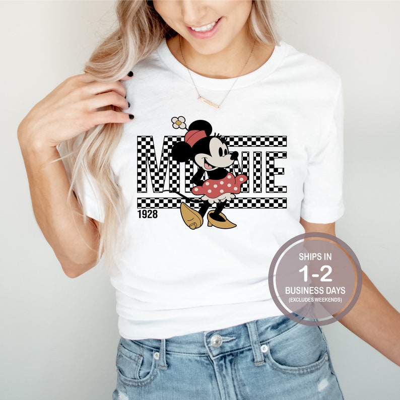 May include: White t-shirt with a black and white checkered design featuring a cartoon image of Minnie Mouse in a red dress with white polka dots. The text "MINNIE" is written in black letters above the image and the year "1928" is written below the image.