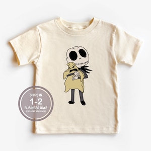May include: A cream colored t-shirt with a cartoon image of Jack Skellington from The Nightmare Before Christmas holding a brown sack with a face. The text "SHIPS IN 1-2 BUSINESS DAYS (EXCLUDES WEEKENDS)" is printed on the shirt.