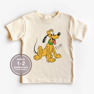 May include: A cream colored short-sleeved t-shirt with a cartoon image of Pluto, a yellow dog with a green collar, printed on the front. The text "Pluto" is written in black cursive below the image.