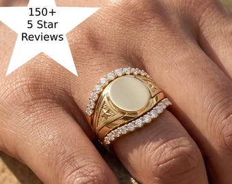 Puede incluir: Un anillo de sello de oro con una cara circular lisa, flanqueado por dos bandas delgadas incrustadas con pequeñas piedras claras. Un gráfico en forma de estrella blanca muestra el texto 150+ 5 Star Reviews en negro.
