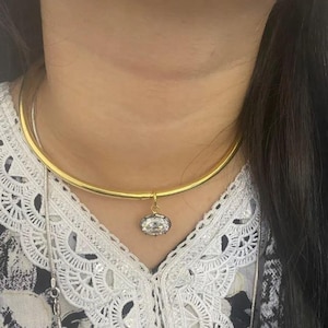 May include: A gold choker necklace with a large, clear, oval-shaped pendant.