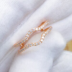 Puede incluir: Un engastador de anillo de oro rosa con un dise&ntilde;o ondulado, que presenta una fila de piedras transparentes brillantes a cada lado.