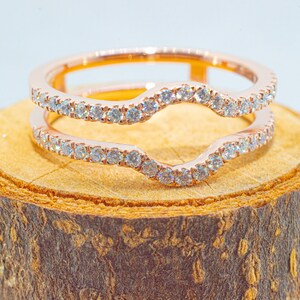 Puede incluir: Un anillo de oro rosa con un dise&ntilde;o abierto y curvo, engastado con peque&ntilde;os diamantes. El anillo est&aacute; sobre una superficie de madera.