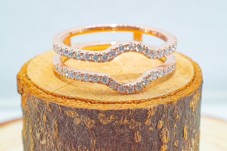 Puede incluir: Un anillo de oro rosa con un dise&ntilde;o abierto y curvo, engastado con peque&ntilde;os diamantes. El anillo est&aacute; sobre una superficie de madera.