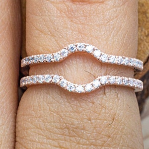 Puede incluir: Dos delicadas alianzas curvas con una fila de brillantes diamantes engastados en una banda de oro rosa.