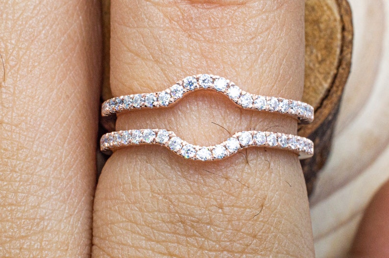 Puede incluir: Dos delicadas alianzas curvas con una fila de brillantes diamantes engastados en una banda de oro rosa.