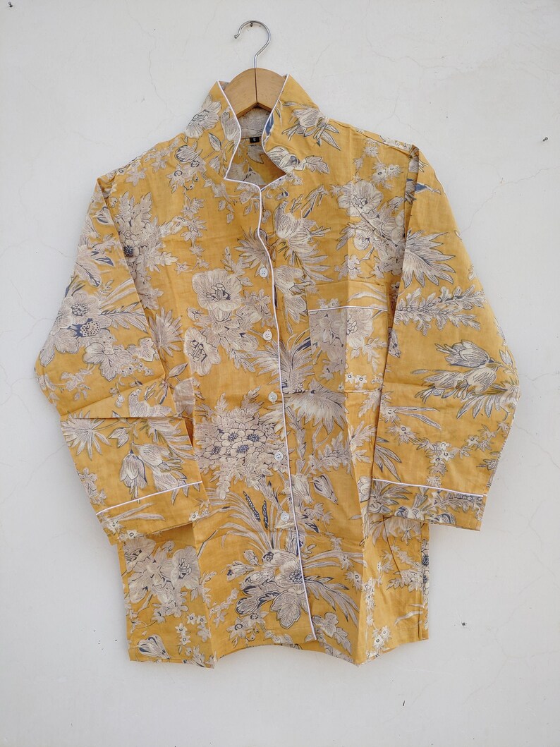May include: A yellow button-up shirt with a floral print and white trim. The shirt has a collar and long sleeves.