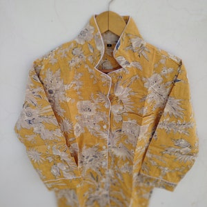 May include: A yellow button-up shirt with a white floral print and white trim. The shirt has a mandarin collar and long sleeves.