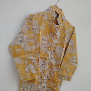 May include: A yellow long-sleeved shirt with a white floral pattern. The shirt has a mandarin collar and a button-up front.