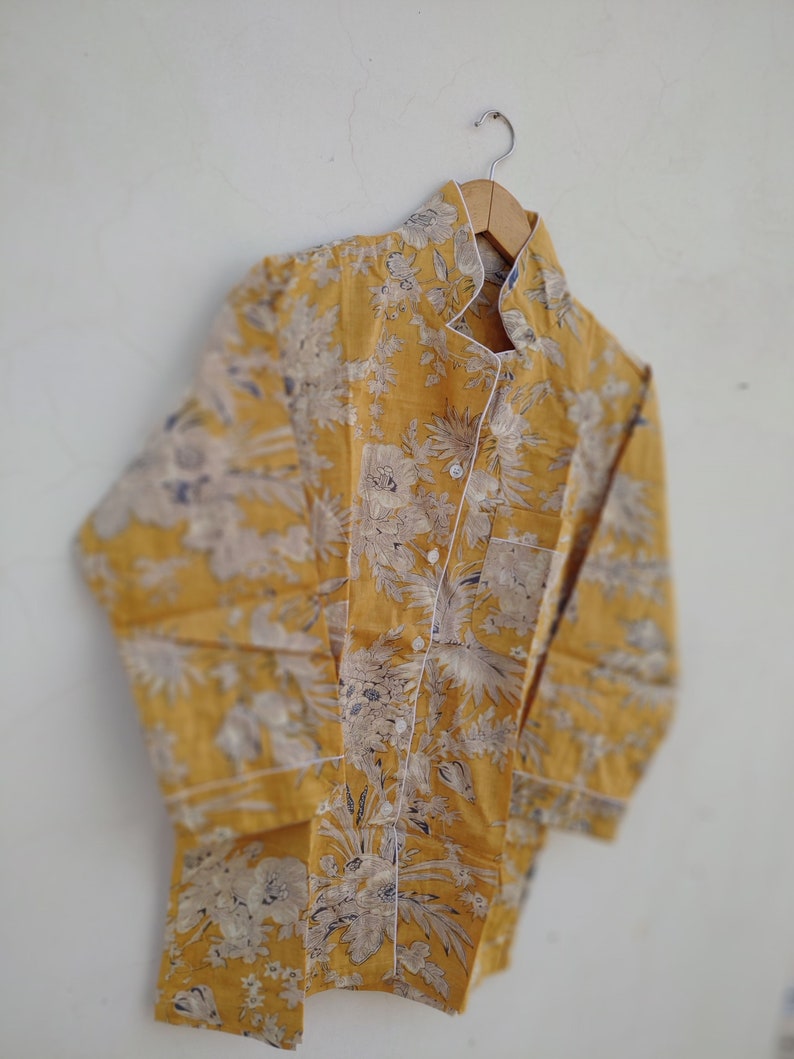 May include: A yellow long-sleeved shirt with a white floral pattern. The shirt has a mandarin collar and a button-up front.