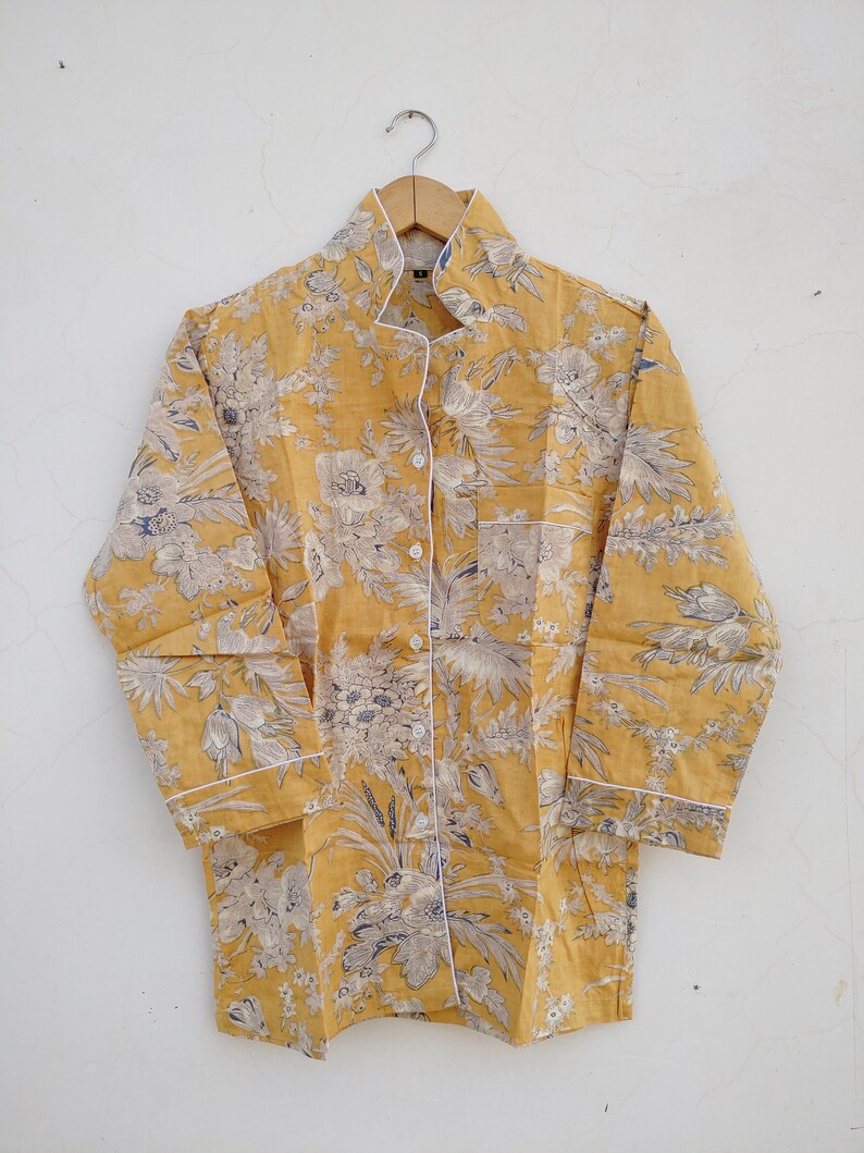 May include: A yellow button-up shirt with a floral print and white trim. The shirt has a collar and long sleeves.