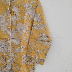May include: A yellow long-sleeved shirt with a white floral print. The shirt has a button-up front and a pocket on the left side.