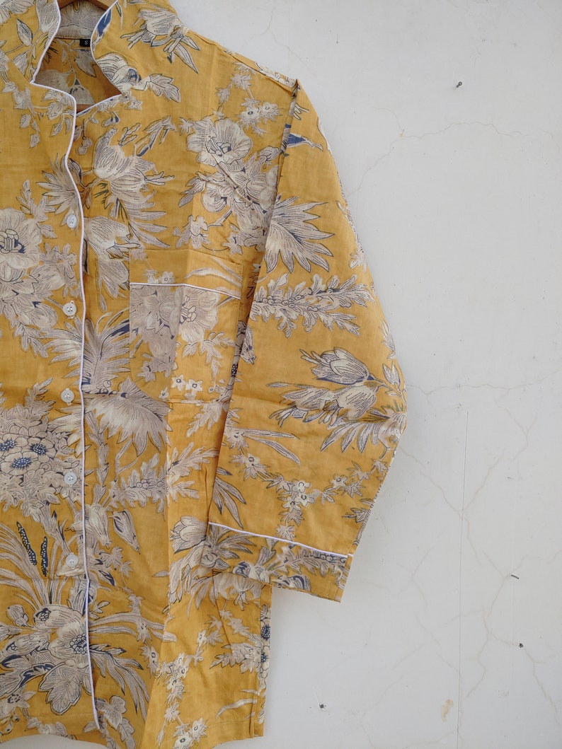 May include: A yellow long-sleeved shirt with a white floral print. The shirt has a button-up front and a pocket on the left side.