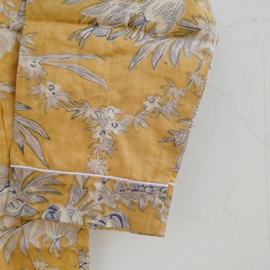 May include: A yellow fabric with a white and blue floral print. The fabric has a white trim around the edge.