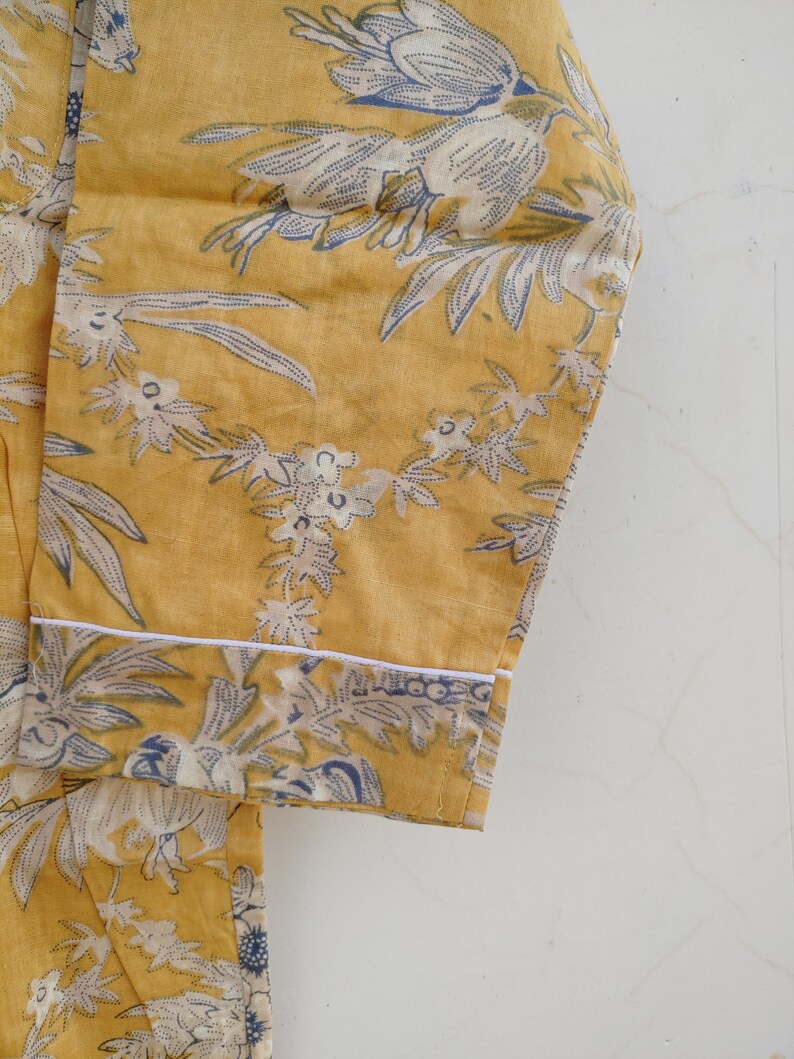 May include: A yellow fabric with a white and blue floral print. The fabric has a white trim around the edge.