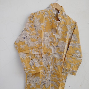 May include: A yellow button-up shirt with a floral print and white trim. The shirt has a mandarin collar and long sleeves.