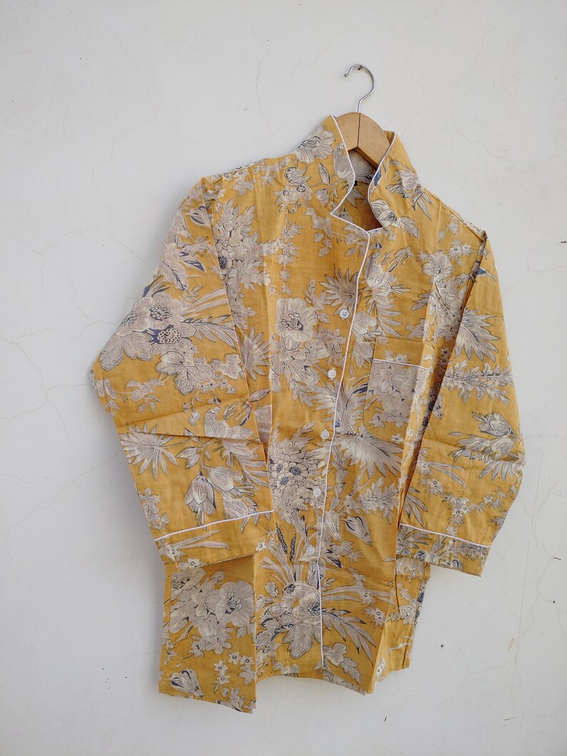 May include: A yellow button-up shirt with a floral print and white trim. The shirt has a mandarin collar and long sleeves.
