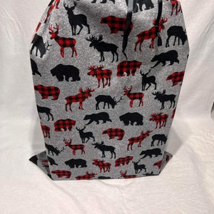 May include: A grey and red plaid Christmas gift bag with black silhouettes of deer, moose, and bears. The bag has a black ribbon.