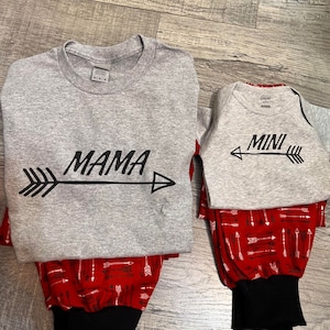 May include: A gray long-sleeve shirt with the word "MAMA" and an arrow printed on it, and a gray short-sleeve shirt with the word "MINI" and an arrow printed on it. Both shirts are paired with red pants with a white arrow pattern.
