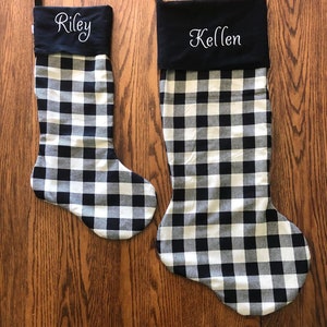 May include: Two black and white buffalo check Christmas stockings with black felt cuffs. The cuff of the stocking on the left has the name "Riley" embroidered on it. The cuff of the stocking on the right has the name "Kellen" embroidered on it.