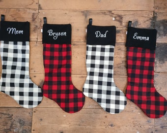 May include: Four red and black buffalo plaid Christmas stockings with black felt cuffs. The cuffs are embroidered with the names "Mom", "Bryson", "Dad", and "Emma".