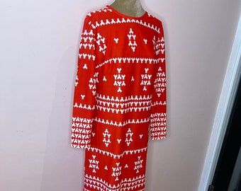 Può includere: Un lungo vestito rosso con un motivo geometrico bianco. Il vestito ha maniche lunghe e una scollatura rotonda.