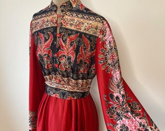May include: A long red maxi dress with a black and red patterned bodice and bell sleeves. The bodice has a high neck and a button closure at the front.