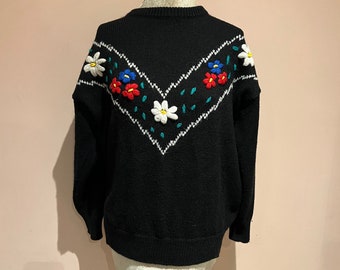 May include: Black knitted sweater with a white, red, blue, and green embroidered floral design.