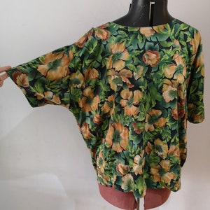 May include: A green and orange floral print top with short sleeves. The top has a relaxed fit and a round neckline.