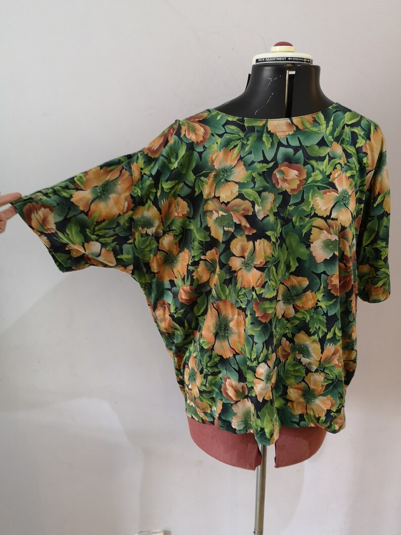 May include: A green and orange floral print top with short sleeves. The top has a relaxed fit and a round neckline.