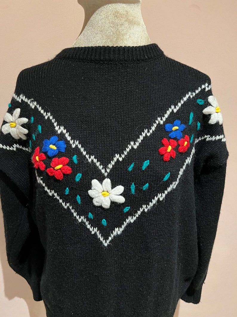 May include: Black knitted sweater with a white, blue, red, and green embroidered floral design on the front.