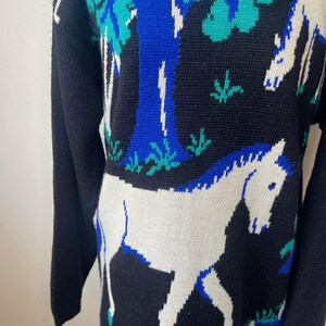 May include: Black knitted sweater with a white horse and blue tree design.