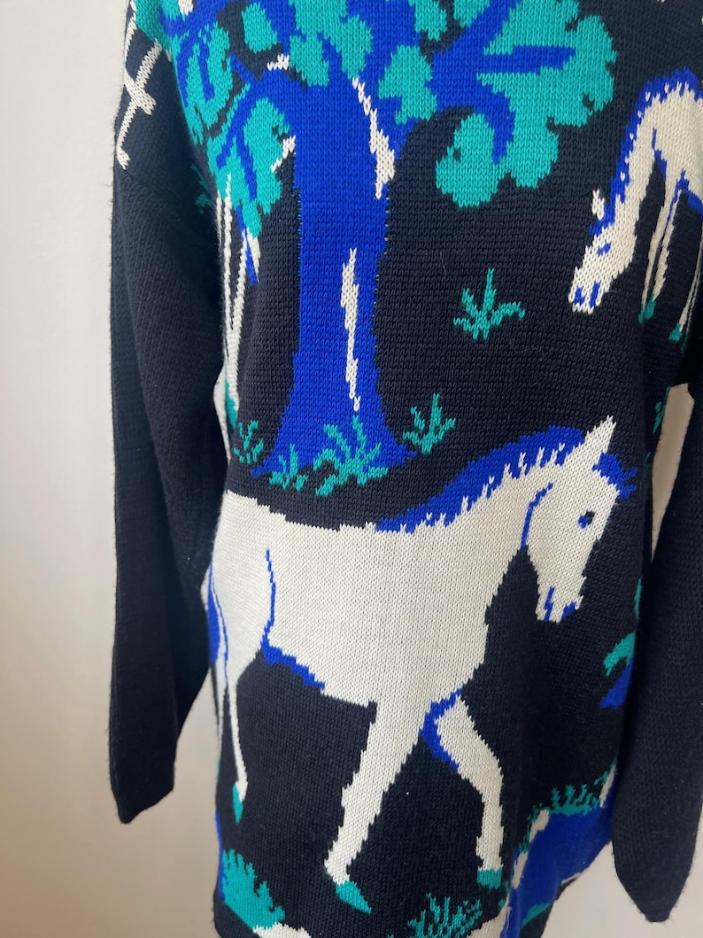 May include: Black knitted sweater with a white horse and blue tree design.