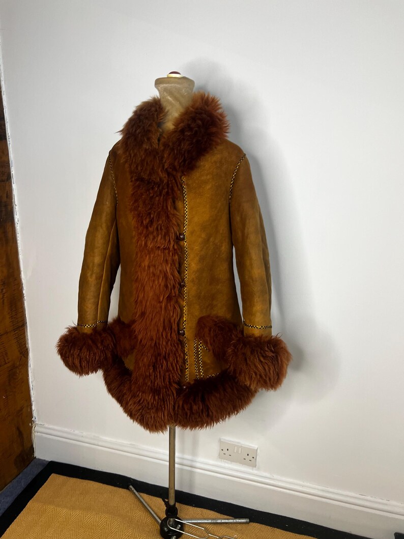 May include: A vintage brown suede coat with a faux fur collar, cuffs, and trim. The coat features a button-up front and decorative stitching. The coat is displayed on a mannequin.