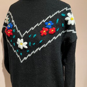 May include: Black knitted sweater with a white and teal chevron pattern and embroidered flowers in red, blue, and white.