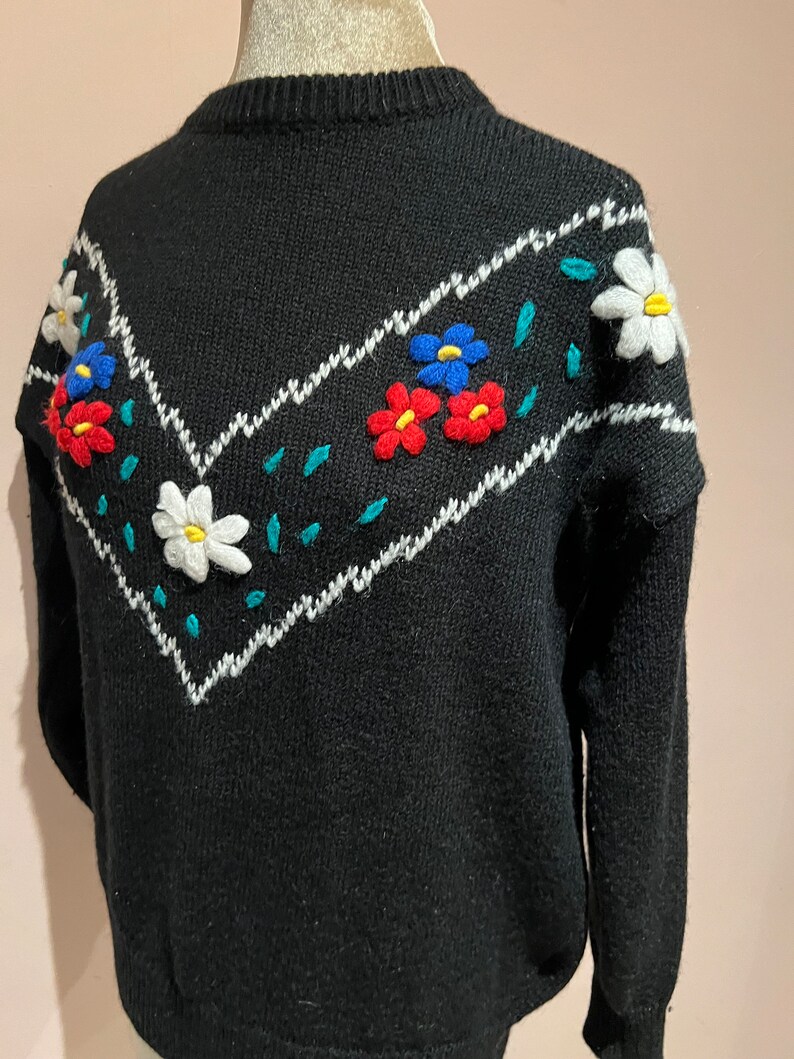 May include: Black knitted sweater with a white and teal chevron pattern and embroidered flowers in red, blue, and white.