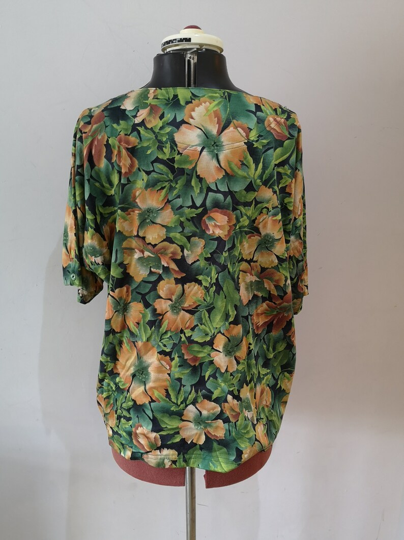 May include: A green, orange, and brown floral print blouse with short sleeves.