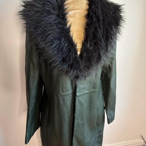 May include: A dark green leather coat with a black faux fur collar. The coat is long, reaching the mid-calf, and has a classic, tailored design. The collar adds a touch of luxury to the outerwear.