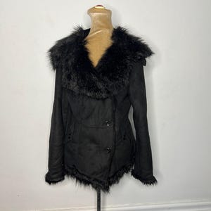 May include: A black faux fur collared jacket with a double breasted closure and a fur trim around the bottom hem.