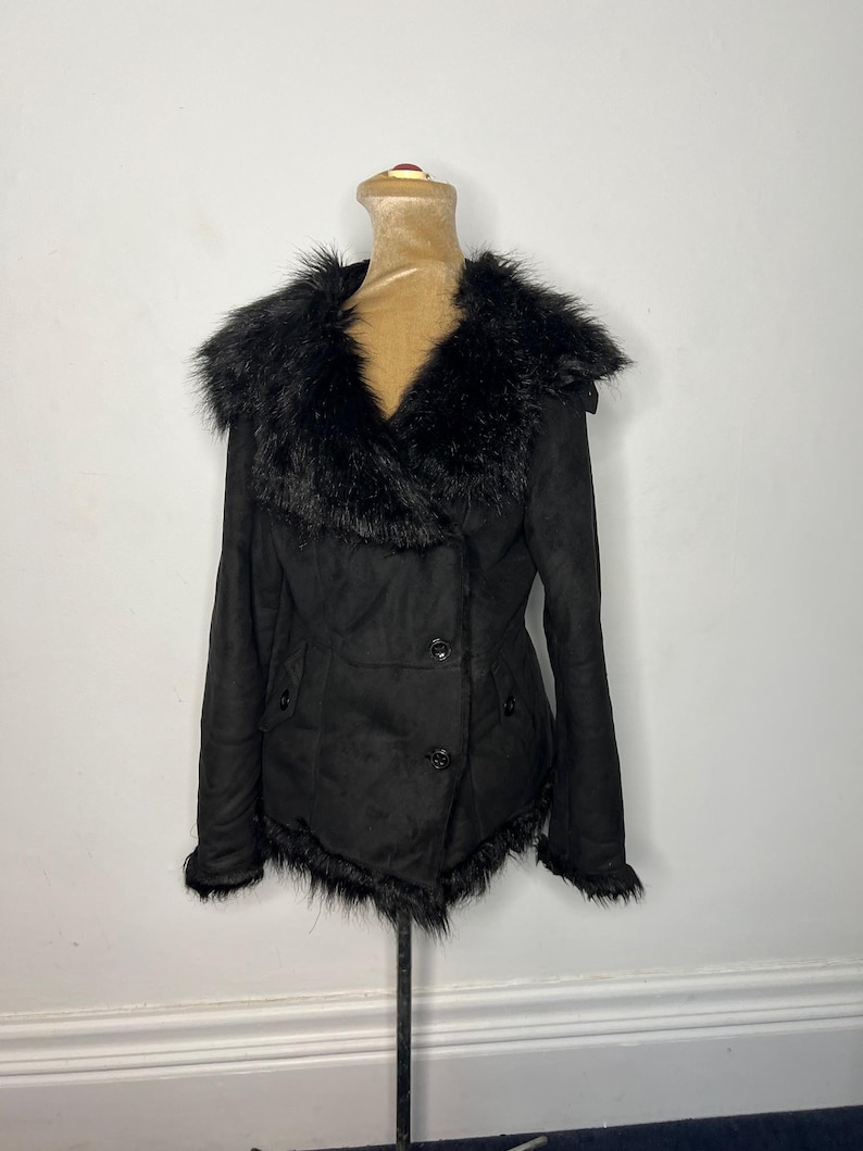 May include: A black faux fur collared jacket with a double breasted closure and a fur trim around the bottom hem.