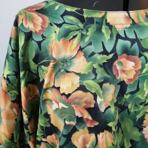 May include: A black and green floral print blouse with orange flowers. The blouse has a scoop neck and short sleeves.